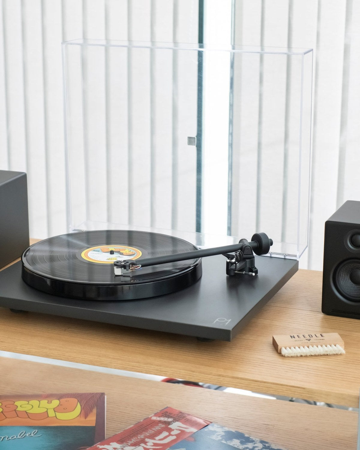 Tornamesa Rega Planar 1 con parlantes Audioengine A2+ sobre un mueble de roble, junto a una escobilla Needle y vinilos